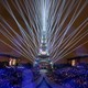 Lasers light up the sky around the Eiffel Tower, watched by a crowd at the Olympics opening ceremony.