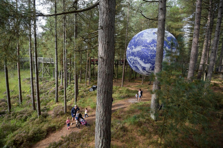 A huge inflatable Earth is suspended in a forested park.
