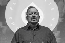 2 black-and-white photos: standing man with eyes closed praying in front of "Floodgate" screen; man preaching to small congregation from podium with cross behind