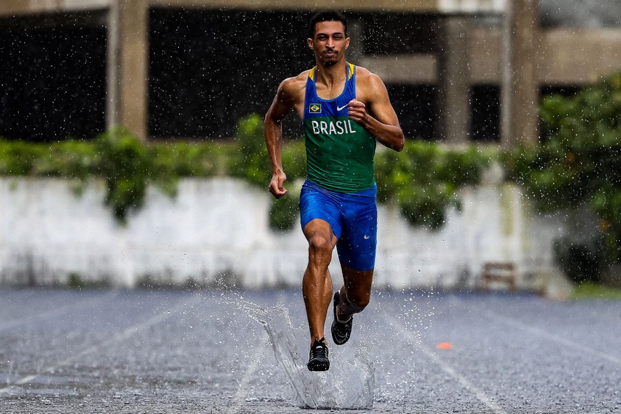 A man runs down a track during a heavy downpour, splashing as he steps.