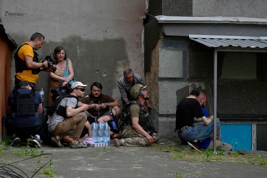 Eight or nine people crouch beside a wall.