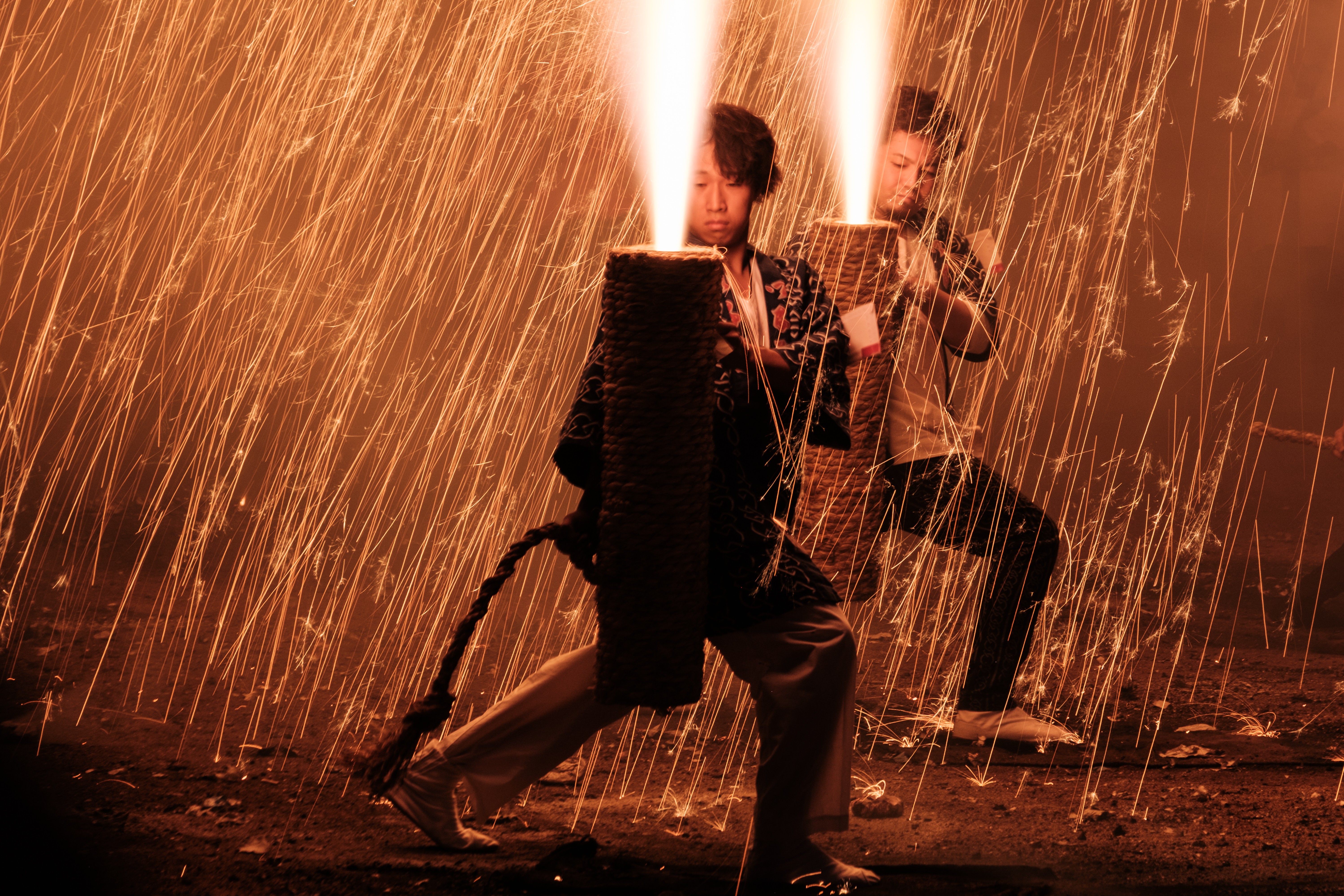 Two people hold traditional hand-held fireworks during a festival, with sparks raining down on them.
