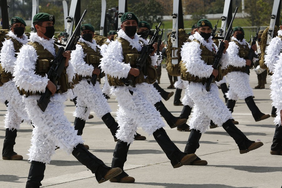 Chilean soldiers march together while wearing white frilly uniforms.