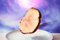 Picture of a piece of meat floating above a table with a purple background behind it