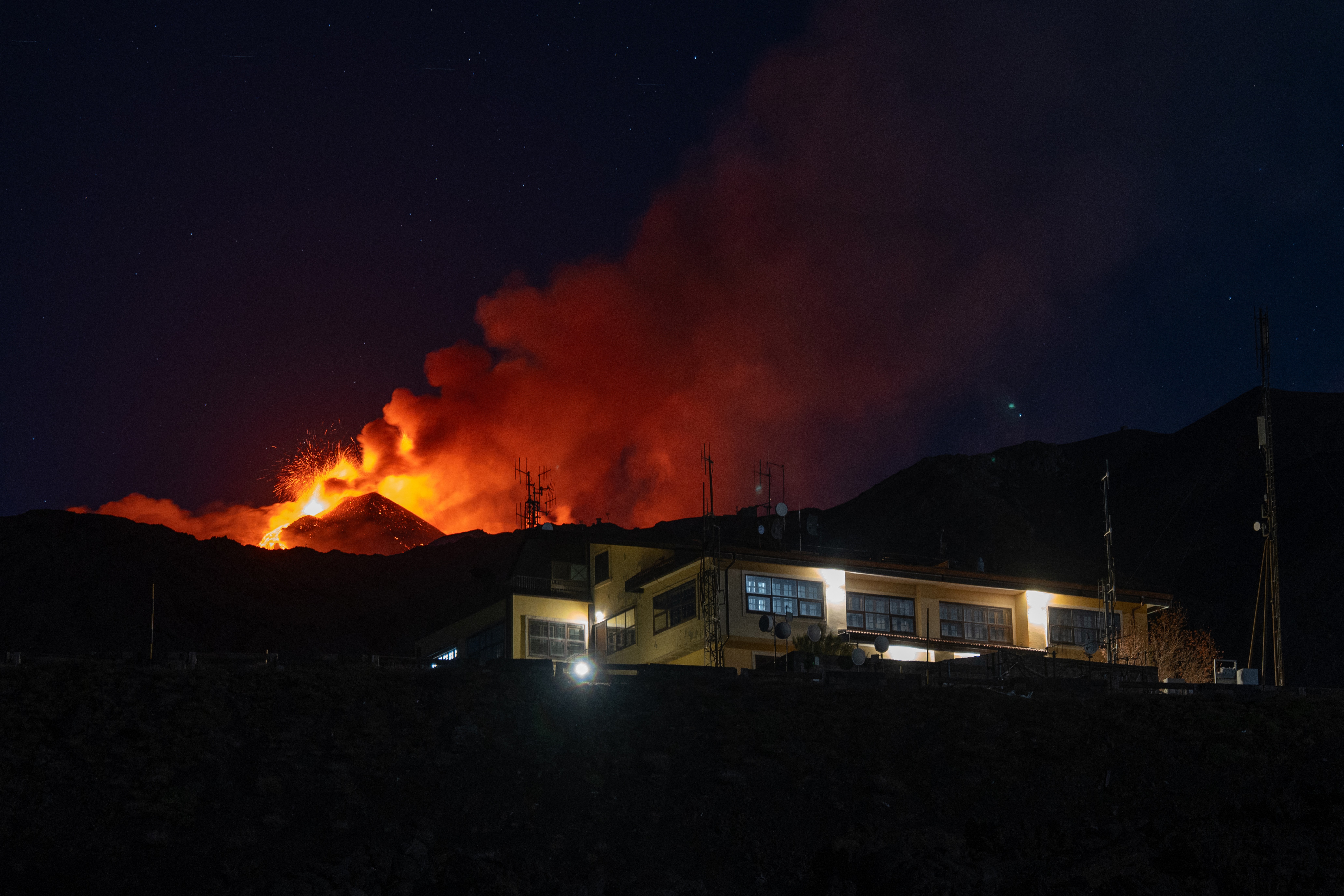 Lava flows behind a house at night, during an eruption.