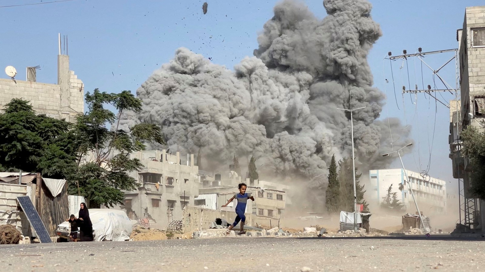 A girl runs across a street, as smoke rises in the background from an airstrike in Gaza.