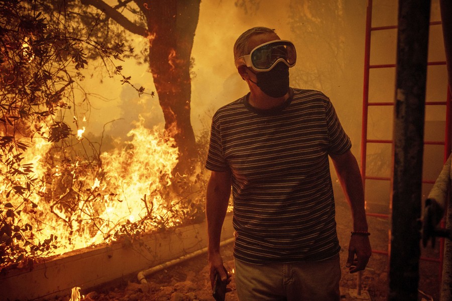 A civilian wearing a mask and goggles walks near an active brush fire.