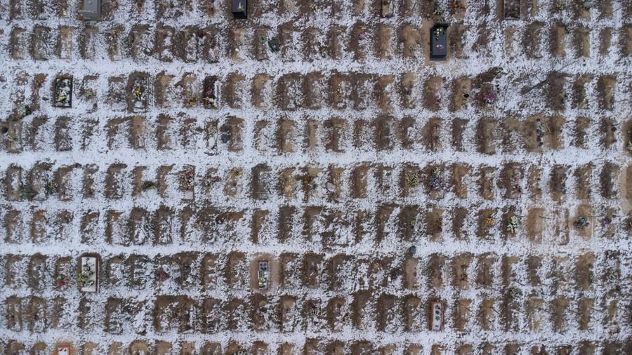 A drone view of dozens of graves dug side by side, dusted with snow.