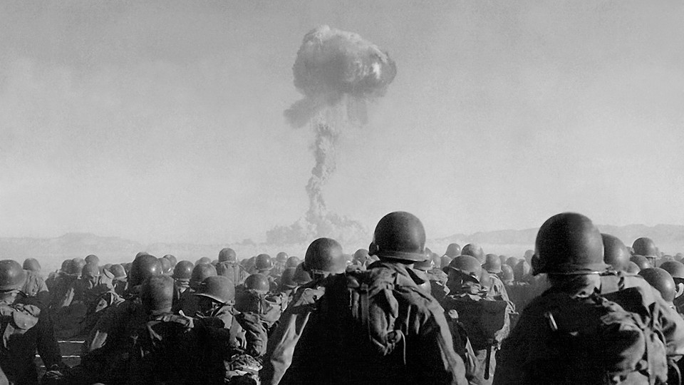 A group of troops watch a plume of smoke rise in the sky.