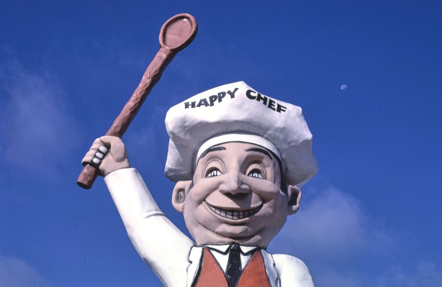 A large statue of a smiling chef holds a huge wooden spoon aloft.