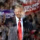 Donald Trump smiles behind a window of bulletproof glass that reflects his cheering supporters and signs