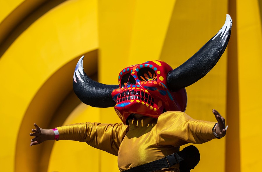 A performer dances while wearing a large skull mask with horns.
