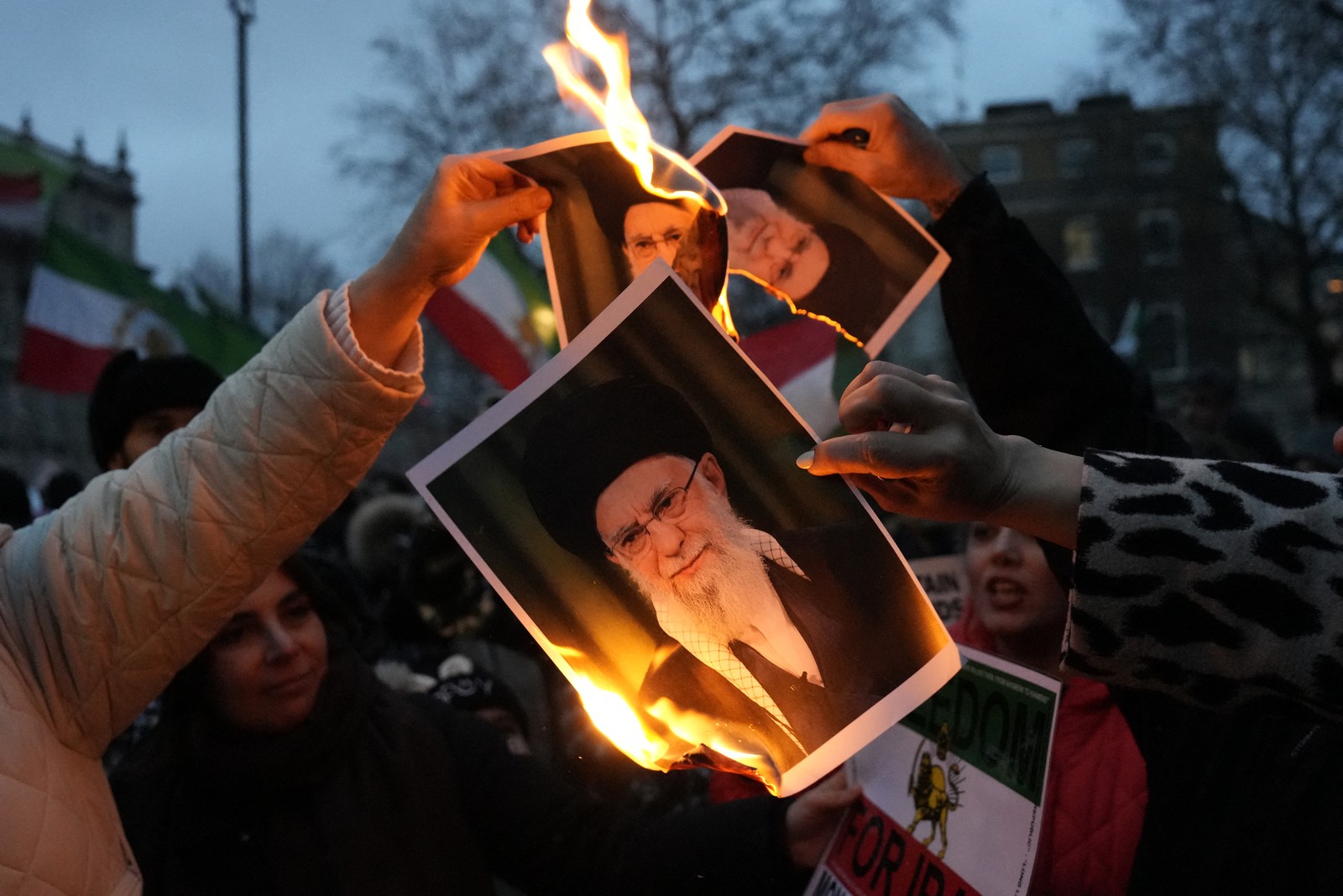 Protesters burn several photographs of Iranian leader Ayatollah Ali Khamenei.