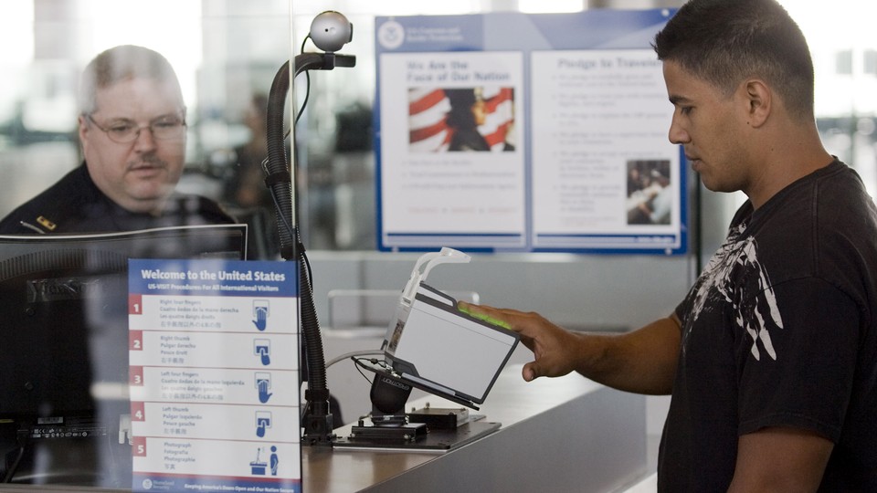 A traveler scans his fingerprints at the Houston airport as a customs officer monitors his computer.