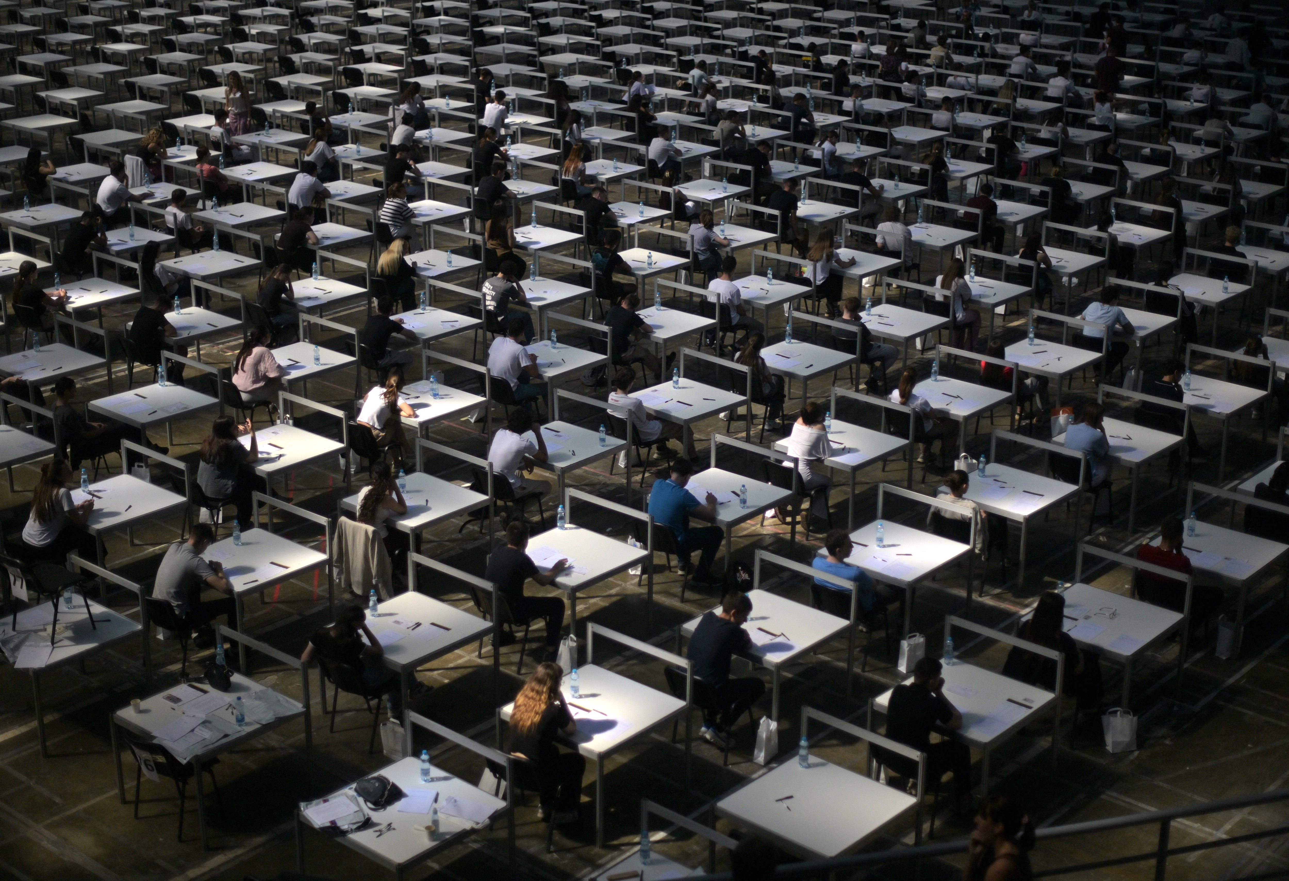 Students sit at dozens of desks set up in a large grid pattern.