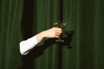 A hand holding a martini glass sticks out from the green curtains