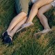A photograph of two sets of legs in the grass, knees facing one another