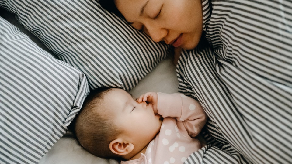 A mother sleeps in a bed next to her baby.