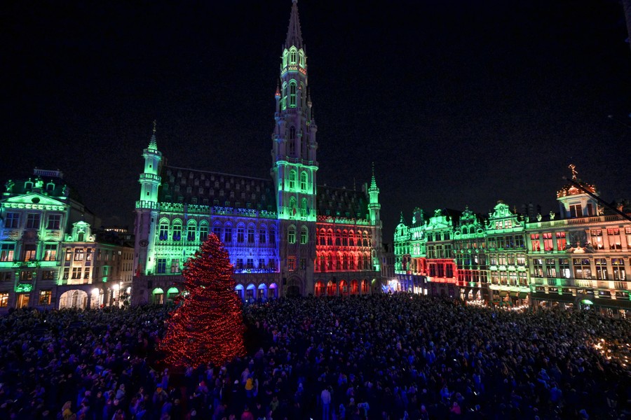An elevated view of a large crowd in a square, surrounded by illuminated buildings and holiday lights