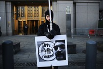 A man dressed in black holds a sign with a symbol for bitcoin