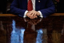 Photograph of Trump from the neck down with his hands on his desk in he