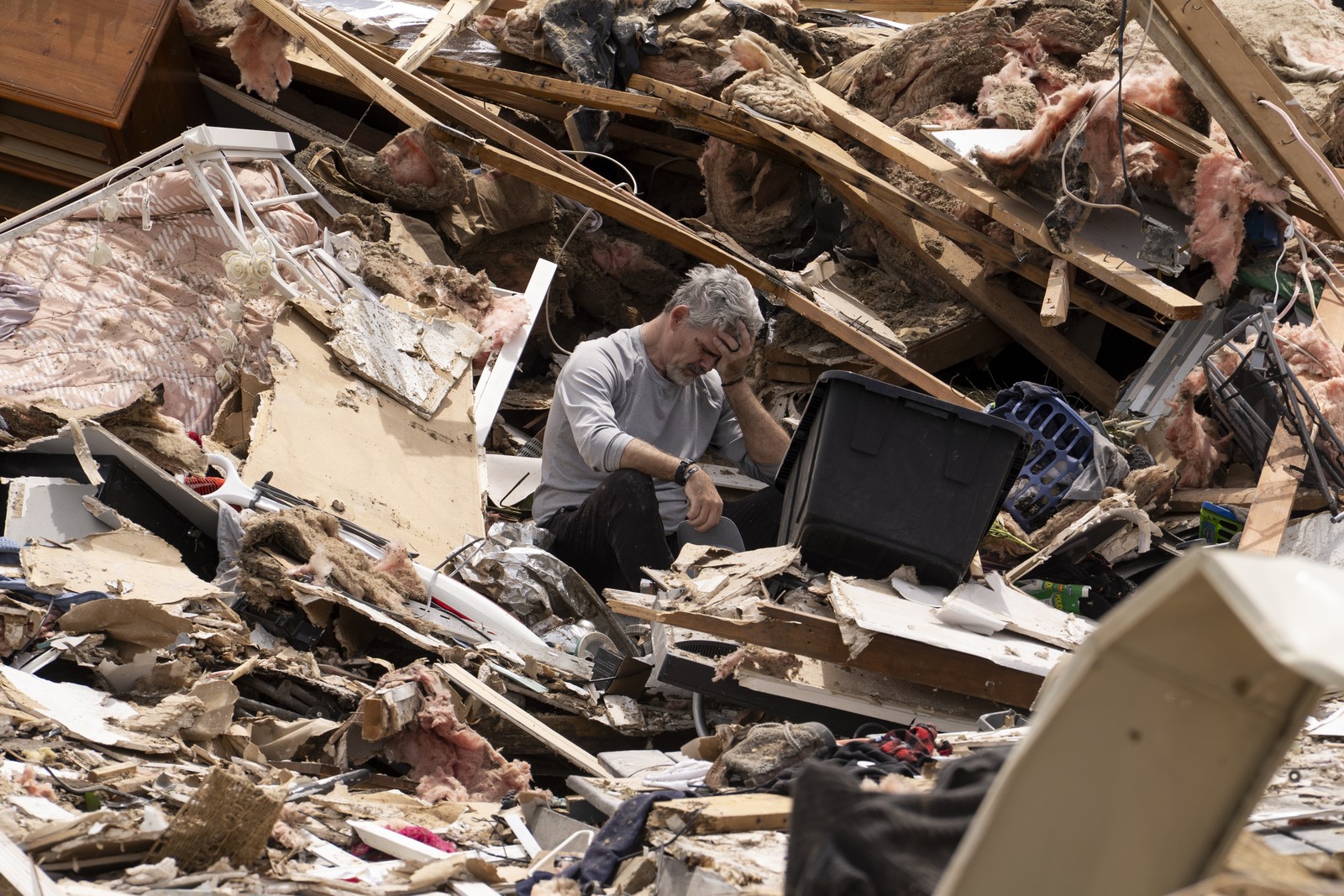 A man holds his head in his hands, sitting on a large pile of debris from a destroyed house.
