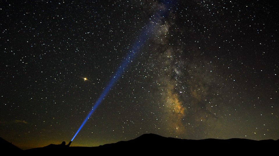 A person shines a flashlight toward the Milky Way in the night sky.