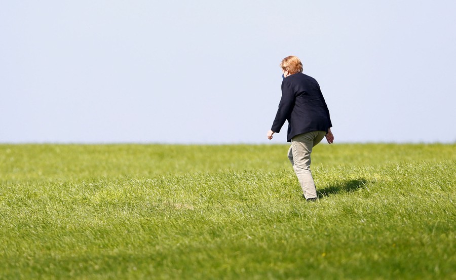 German Chancellor Angela Merkel walks on a grassy hill.