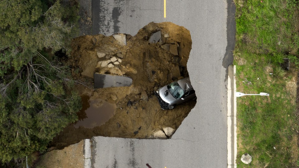 A gray car inside a sinkhole on a roadway
