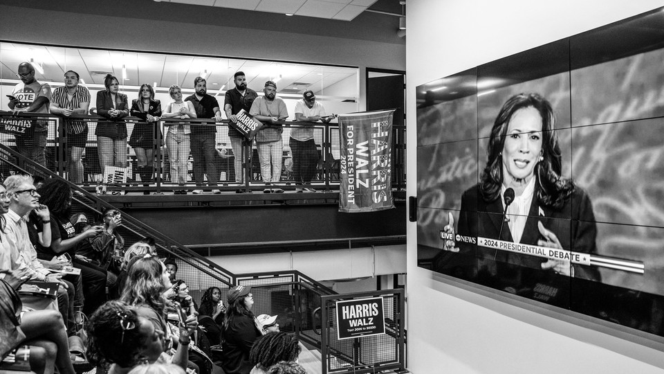 A group of people watch Kamala Harris debating Trump.