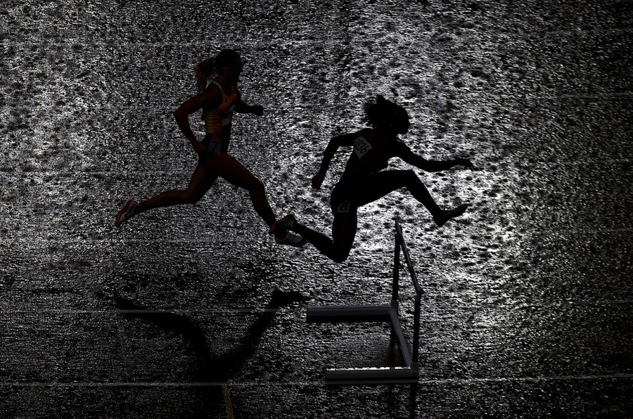Two runners compete on a track during a rainstorm.