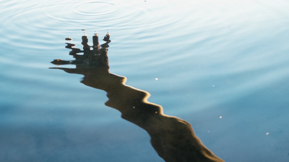 A hand reflected in ripples across blue water