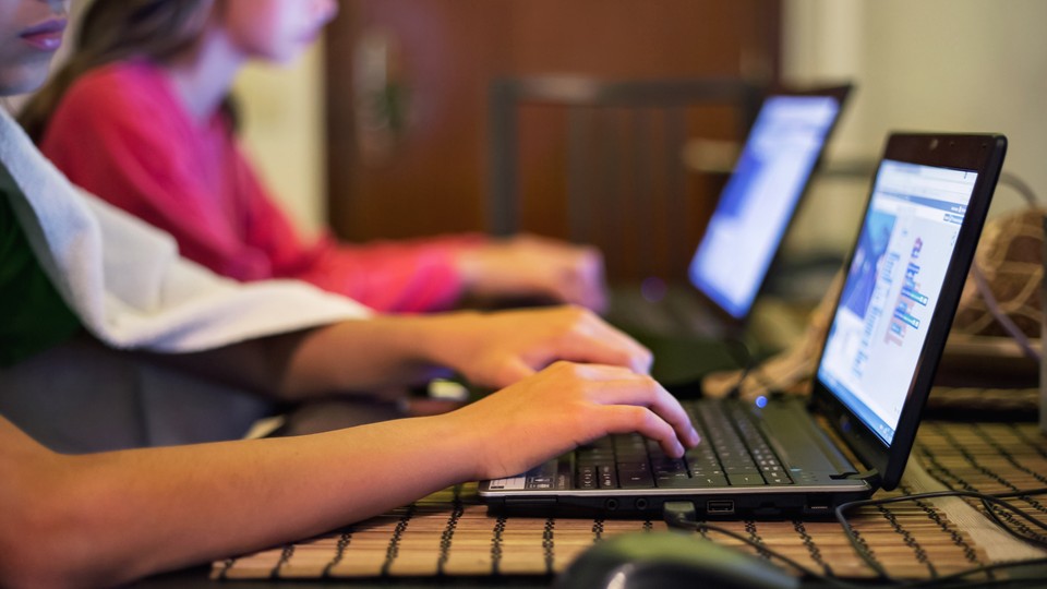 Two sets of hands typing on two black computers