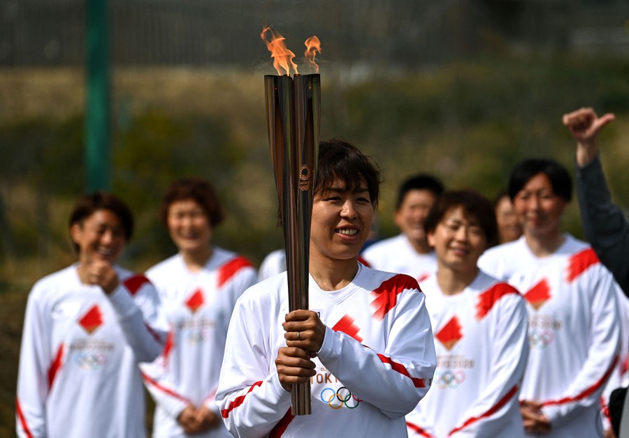 A person holds a lit Olympic torch, as a half-dozen teammates watch in the background.
