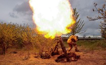 A bright flash of fire blazes above a mortar launcher as a soldier ducks nearby.