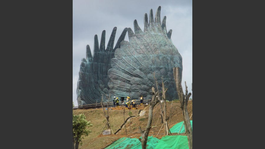 Workers stand near a large sculpture of a pair of outstretched bird's wings.