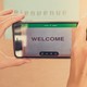 Hands hold a smartphone in front of a sign saying "Bienvenue," and the smartphone reads "Welcome."