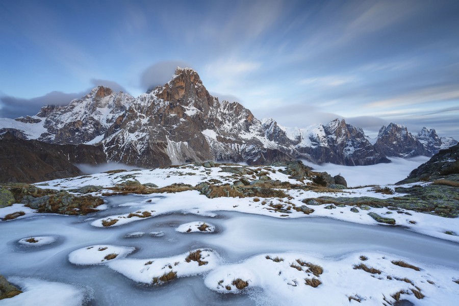 A view of snow and ice on the ground among surrounding snow-covered rocky mountains.