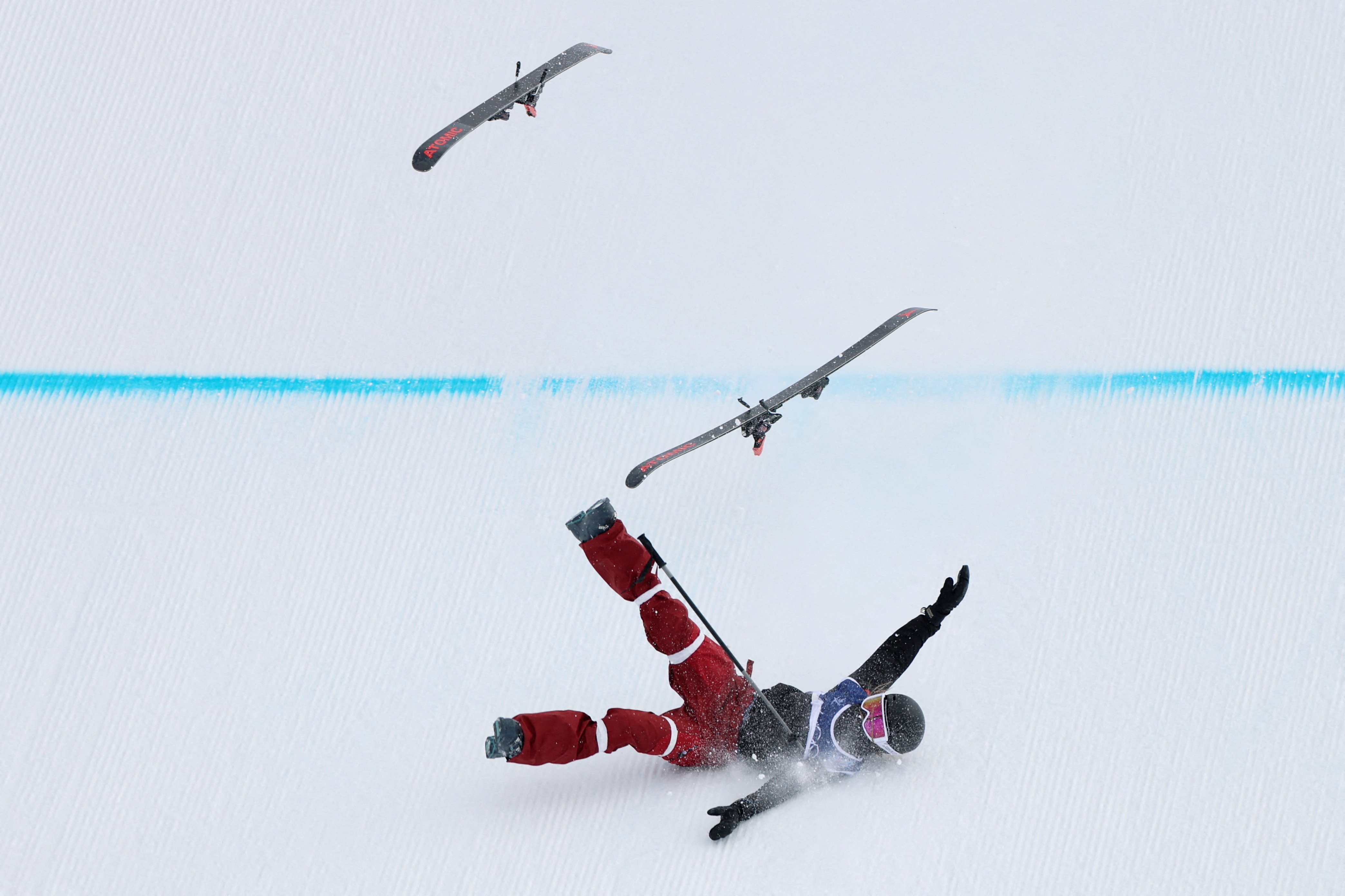 A ski racer falls during a run, their skis flying off into the air.