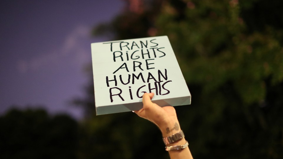 A hand holding a sign that reads "Trans Rights Are Human Rights"