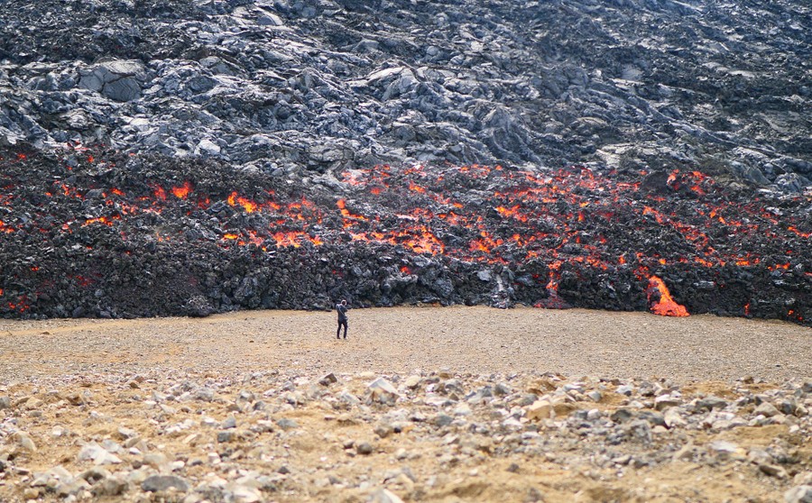 A person stands before a broad lava flow.