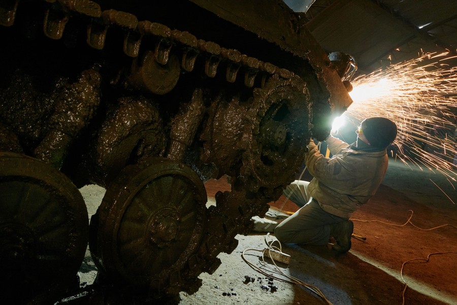 A person works to repair a military tank, using a tool that throws off sparks.