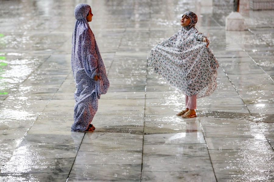 Two young Muslim worshippers stand in the rain at a shrine.