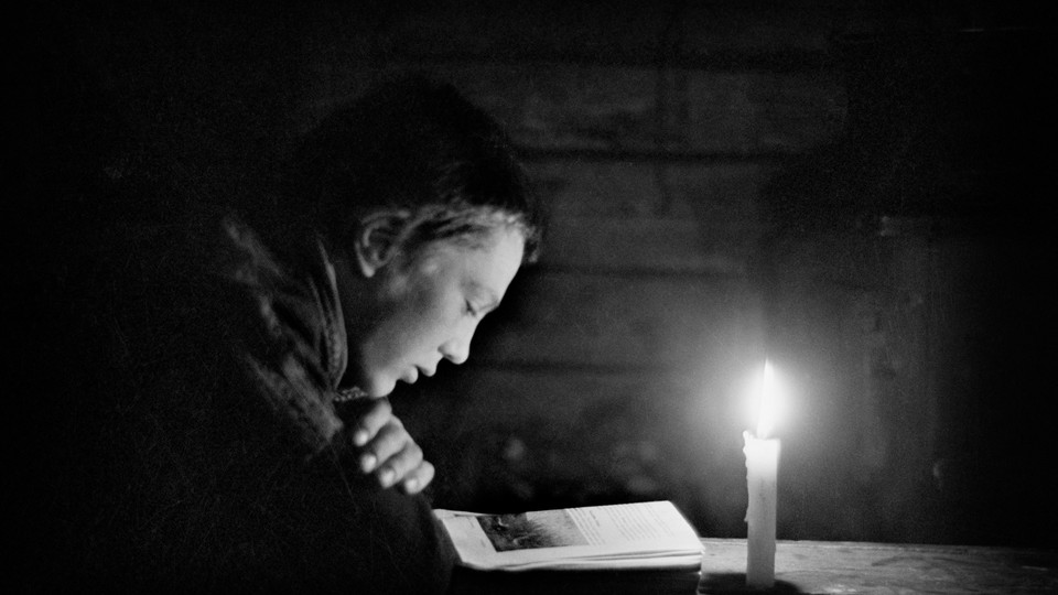 A black-and-white photo of a young boy reading by candlelight
