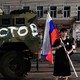 Photograph of a man holding aRussian flag next to an army tank