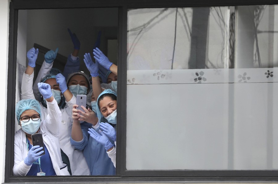 Medical staff lean out a window, raising their arms in support of demonstrators.