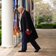 Donald Trump walks out of the White House holding a MAGA hat.