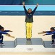 On a medals podium, two gymnasts on either side of the gold-medal winner playfully bow down to her, as she raises her arms.