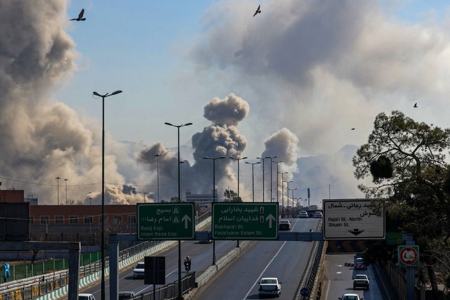 Cars drive on a highway below plumes of smoke