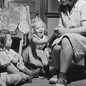 Black-and-white photo of a woman sitting in a chair reading a storybook to three kids seated on the floor